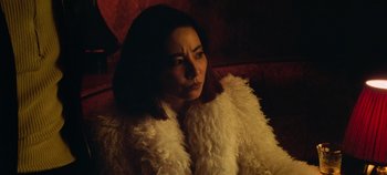 Movie still from “Heart of Stone” (2023), directed by Tom Harper – A woman sitting on a red couch wearing a white coat; Close Up shot, High angle