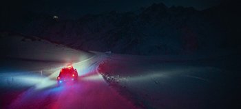Movie still from “Heart of Stone” (2023), directed by Tom Harper – A car driving down a road at night with lights on; Extreme Wide shot, High angle