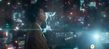 Movie still from “Heart of Stone” (2023), directed by Tom Harper – A woman standing in front of a window with lights; Medium shot, Low angle