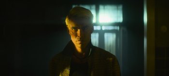 Movie still from “Heart of Stone” (2023), directed by Tom Harper – A man with blonde hair and a jacket on; Close Up shot, Low angle