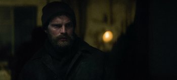 Movie still from “Heart of Stone” (2023), directed by Tom Harper – A man with a beard and a hat is looking at the camera; Close Up shot, Over the shoulder angle