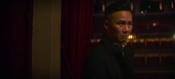 Movie still from “Heart of Stone” (2023), directed by Tom Harper – A man standing in front of a red curtain; Close Up shot, Over the shoulder angle