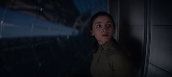 Movie still from “Heart of Stone” (2023), directed by Tom Harper – A young girl looking out of a window at night; Medium shot, Low angle