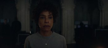 Movie still from “Heart of Stone” (2023), directed by Tom Harper – A woman with curly hair wearing a white shirt; Close Up shot, Over the shoulder angle