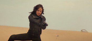 Movie still from “Heart of Stone” (2023), directed by Tom Harper – A woman in a black outfit is holding a gun; Medium shot, Over the shoulder angle