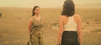 Movie still from “Heart of Stone” (2023), directed by Tom Harper – Two women standing on a dirt field looking at each other; Medium shot, Over the shoulder angle