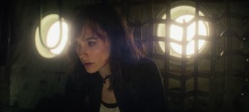 Movie still from “Heart of Stone” (2023), directed by Tom Harper – A woman with long dark hair is looking into the light; Close Up shot, Over the shoulder angle