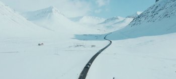 Movie still from “Heart of Stone” (2023), directed by Tom Harper – A car driving down a road in the middle of a snow covered field; Extreme Wide shot, High angle