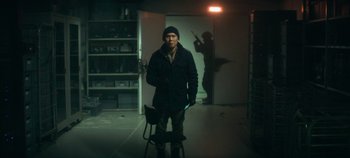 Movie still from “Heart of Stone” (2023), directed by Tom Harper – A man standing in a room with a chair; Medium shot, Over the shoulder angle