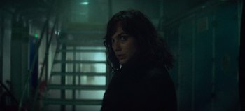 Movie still from “Heart of Stone” (2023), directed by Tom Harper – A woman with long hair standing in a dark room; Close Up shot, Over the shoulder angle