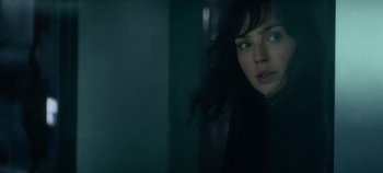 Movie still from “Heart of Stone” (2023), directed by Tom Harper – A woman standing next to a wall in a dark room; Close Up shot, Over the shoulder angle