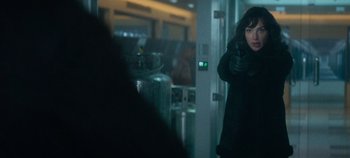 Movie still from “Heart of Stone” (2023), directed by Tom Harper – A woman in a black jacket is pointing at the camera; Medium shot, Over the shoulder angle