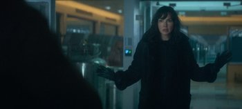 Movie still from “Heart of Stone” (2023), directed by Tom Harper – A woman in a black coat is holding her hand out; Medium shot, Over the shoulder angle