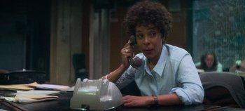 Movie still from “Heart of Stone” (2023), directed by Tom Harper – A woman sitting at a table talking on a phone; Medium shot, Low angle