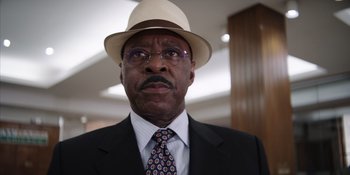 Movie still from “Heist 88” (2023), directed by Menhaj Huda – An older man wearing a hat and a suit; Close Up shot, Low angle