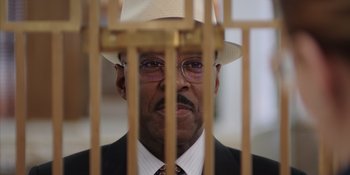 Movie still from “Heist 88” (2023), directed by Menhaj Huda – A person wearing a suit and a hat; Close Up shot, Low angle