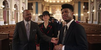 Movie still from “Heist 88” (2023), directed by Menhaj Huda – A group of people standing in front of a building; Medium shot, Over the shoulder angle