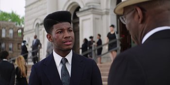 Movie still from “Heist 88” (2023), directed by Menhaj Huda – A young man with a very large black afro haircut; Close Up shot, High angle