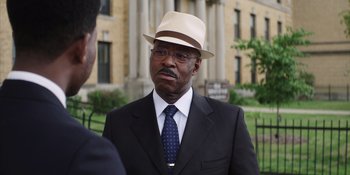 Movie still from “Heist 88” (2023), directed by Menhaj Huda – An older man in a suit and a hat is talking to a man; Close Up shot, Over the shoulder angle