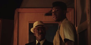 Movie still from “Heist 88” (2023), directed by Menhaj Huda – A man and a man standing next to each other in a room; Close Up shot, Low angle