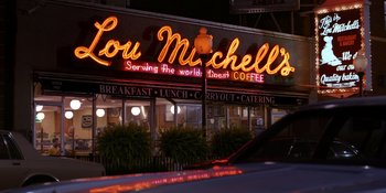 Movie still from “Heist 88” (2023), directed by Menhaj Huda – A neon sign is lit up on the side of a building; Extreme Wide shot, High angle