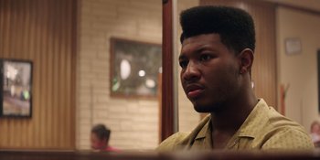 Movie still from “Heist 88” (2023), directed by Menhaj Huda – A young man with a very large black afro haircut; Close Up shot, Over the shoulder angle