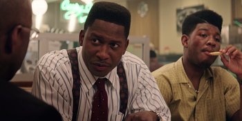 Movie still from “Heist 88” (2023), directed by Menhaj Huda – A person sitting at a table wearing a tie; Close Up shot, Over the shoulder angle