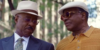 Movie still from “Heist 88” (2023), directed by Menhaj Huda – A couple of men standing next to each other wearing hats; Close Up shot, Low angle