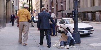 Movie still from “Heist 88” (2023), directed by Menhaj Huda – A man sitting on the side of the road next to another man on the side of the road; Wide shot, Over the shoulder angle