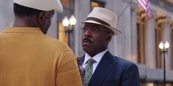 Movie still from “Heist 88” (2023), directed by Menhaj Huda – A man in a suit and tie wearing a hat; Close Up shot, Over the shoulder angle