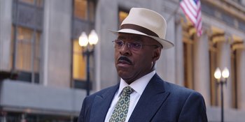 Movie still from “Heist 88” (2023), directed by Menhaj Huda – An older man wearing a hat and a suit; Close Up shot, Over the shoulder angle