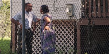 Movie still from “Heist 88” (2023), directed by Menhaj Huda – A man and a woman standing next to each other in front of a chain link fence; Medium shot, Over the shoulder angle