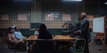 Movie still from “Heist 88” (2023), directed by Menhaj Huda – A woman sitting at a wooden table in front of two men; Wide shot, Over the shoulder angle