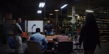 Movie still from “Heist 88” (2023), directed by Menhaj Huda – A group of people sitting at a table in a room; Wide shot, High angle