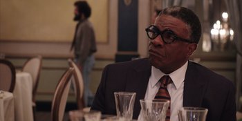 Movie still from “Heist 88” (2023), directed by Menhaj Huda – A man sitting at a dinner table with his eyes wide open; Close Up shot, Over the shoulder angle