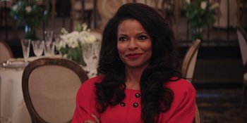 Movie still from “Heist 88” (2023), directed by Menhaj Huda – A woman in a red dress smiling for the camera; Close Up shot, Over the shoulder angle