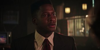 Movie still from “Heist 88” (2023), directed by Menhaj Huda – A man wearing a suit and tie in a dark room; Close Up shot, Low angle