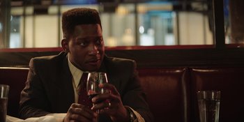 Movie still from “Heist 88” (2023), directed by Menhaj Huda – A man sitting at a table holding a glass of wine; Close Up shot, Over the shoulder angle