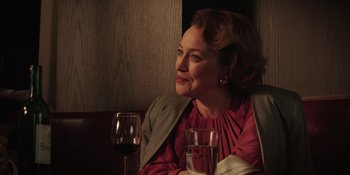 Movie still from “Heist 88” (2023), directed by Menhaj Huda – A woman sitting at a table with a glass of red wine; Close Up shot, Over the shoulder angle