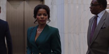 Movie still from “Heist 88” (2023), directed by Menhaj Huda – A woman in a green suit stands in front of a white building; Close Up shot, Low angle