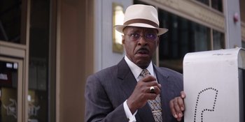 Movie still from “Heist 88” (2023), directed by Menhaj Huda – A man in a suit and a hat is holding a cigarette; Close Up shot, Low angle