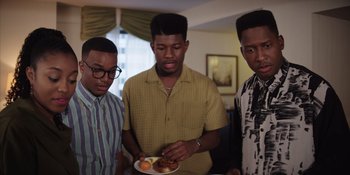 Movie still from “Heist 88” (2023), directed by Menhaj Huda – A group of young men standing around a plate of food; Medium shot, Low angle