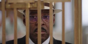 Movie still from “Heist 88” (2023), directed by Menhaj Huda – A person behind bars wearing a suit and a hat; Extreme Close Up shot, Low angle