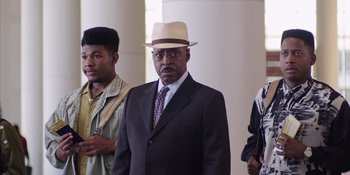 Movie still from “Heist 88” (2023), directed by Menhaj Huda – An older man in a suit and a hat; Medium shot, Low angle