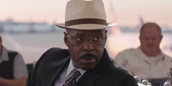 Movie still from “Heist 88” (2023), directed by Menhaj Huda – An older man wearing a hat and glasses; Close Up shot, Over the shoulder angle