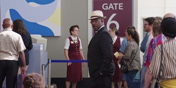 Movie still from “Heist 88” (2023), directed by Menhaj Huda – A man in a suit and a hat standing in front of two other people; Medium shot, Over the shoulder angle