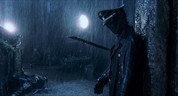 Movie still from “Hellboy” (2004), directed by Guillermo del Toro – A man in a black jacket holding a sword in the rain; Medium shot, High angle