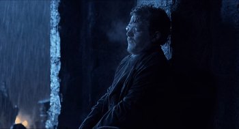 Movie still from “Hellboy” (2004), directed by Guillermo del Toro – A man sitting in a dark room next to a brick wall; Medium shot, Low angle