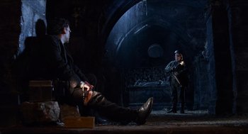 Movie still from “Hellboy” (2004), directed by Guillermo del Toro – A man sitting on the ground next to another man; Wide shot, High angle