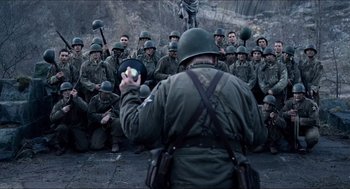 Movie still from “Hellboy” (2004), directed by Guillermo del Toro – A group of men sitting in front of a man holding something; Medium shot, High angle